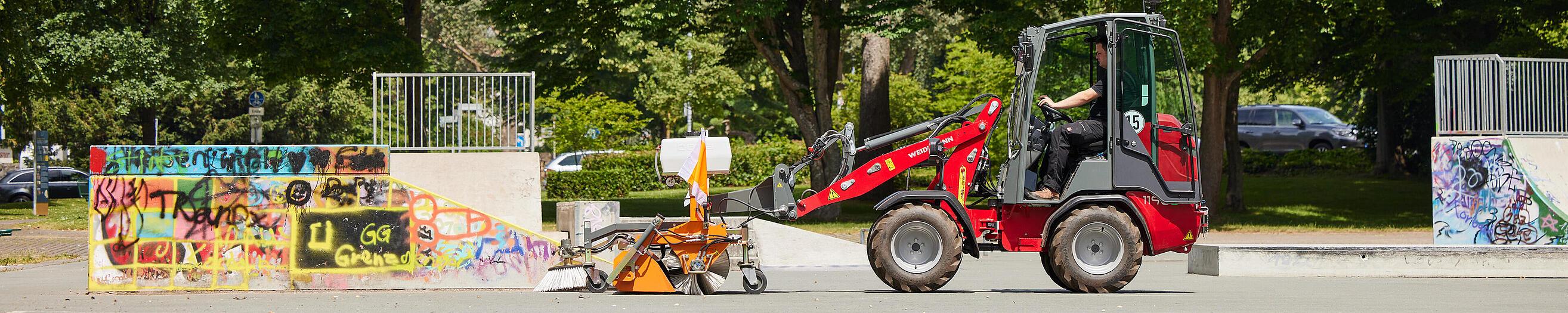 Cabină Weidemann Hoftrac 1190e în parcul orașului cu utilaj de măturat