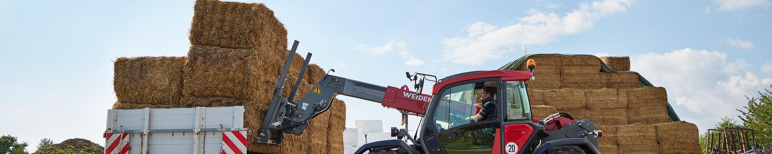 Cargadora telescópica T7035 de Weidemann en acción junto a un remolque de paja